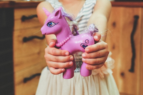 A girl holding a pink toy unicorn.